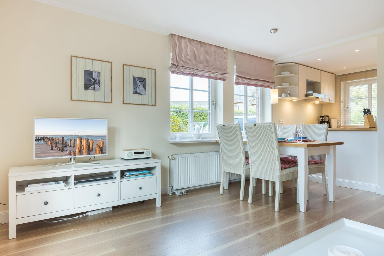 Living and dining area with TV, table and chairs, windows and wooden floor.