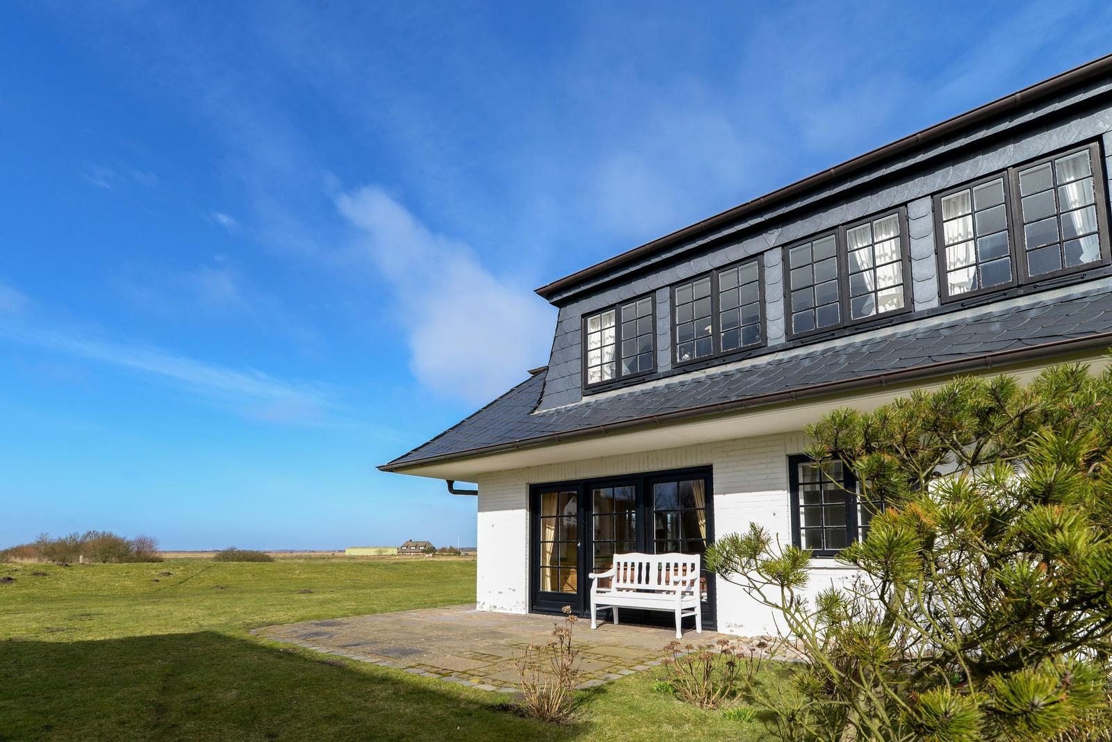 Weiße Villa mit schwarzen Fenstern und Terrasse unter blauem Himmel.
