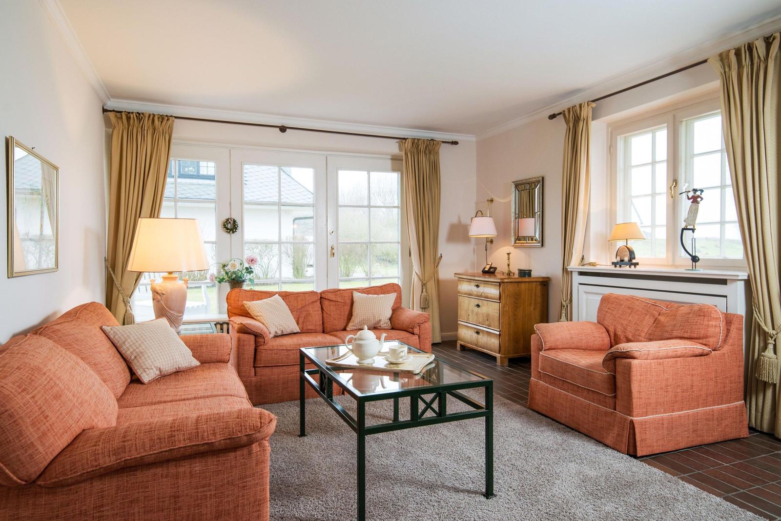 Wohnzimmer mit zwei orangefarbenen Sofas, Glas-Tisch und Holzmöbel.