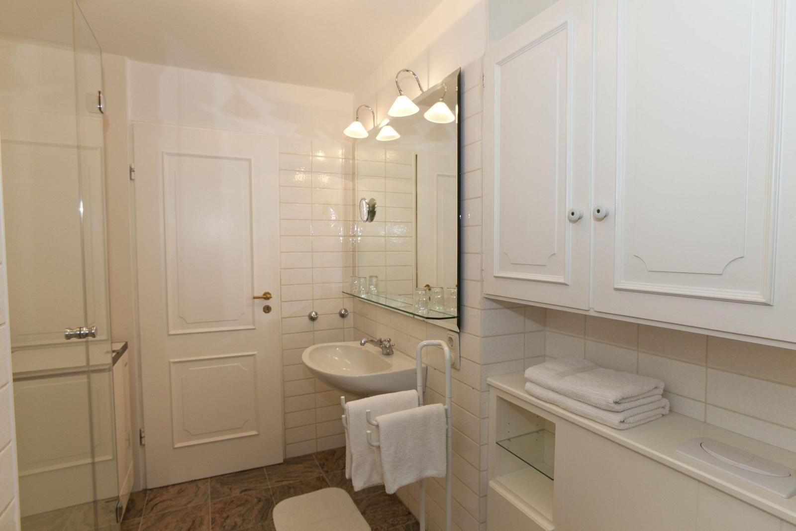 Badezimmer mit Waschbecken, Spiegel, Handtuchhalter und Schränken.