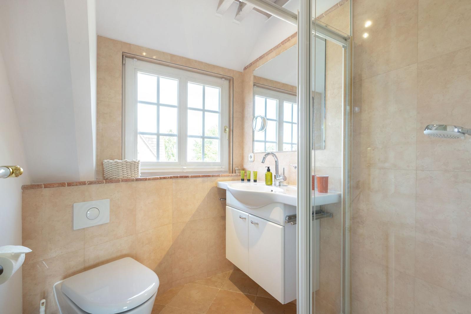 Badezimmer mit Dusche, Waschbecken und Toilette. Fenster mit Blick nach draußen.