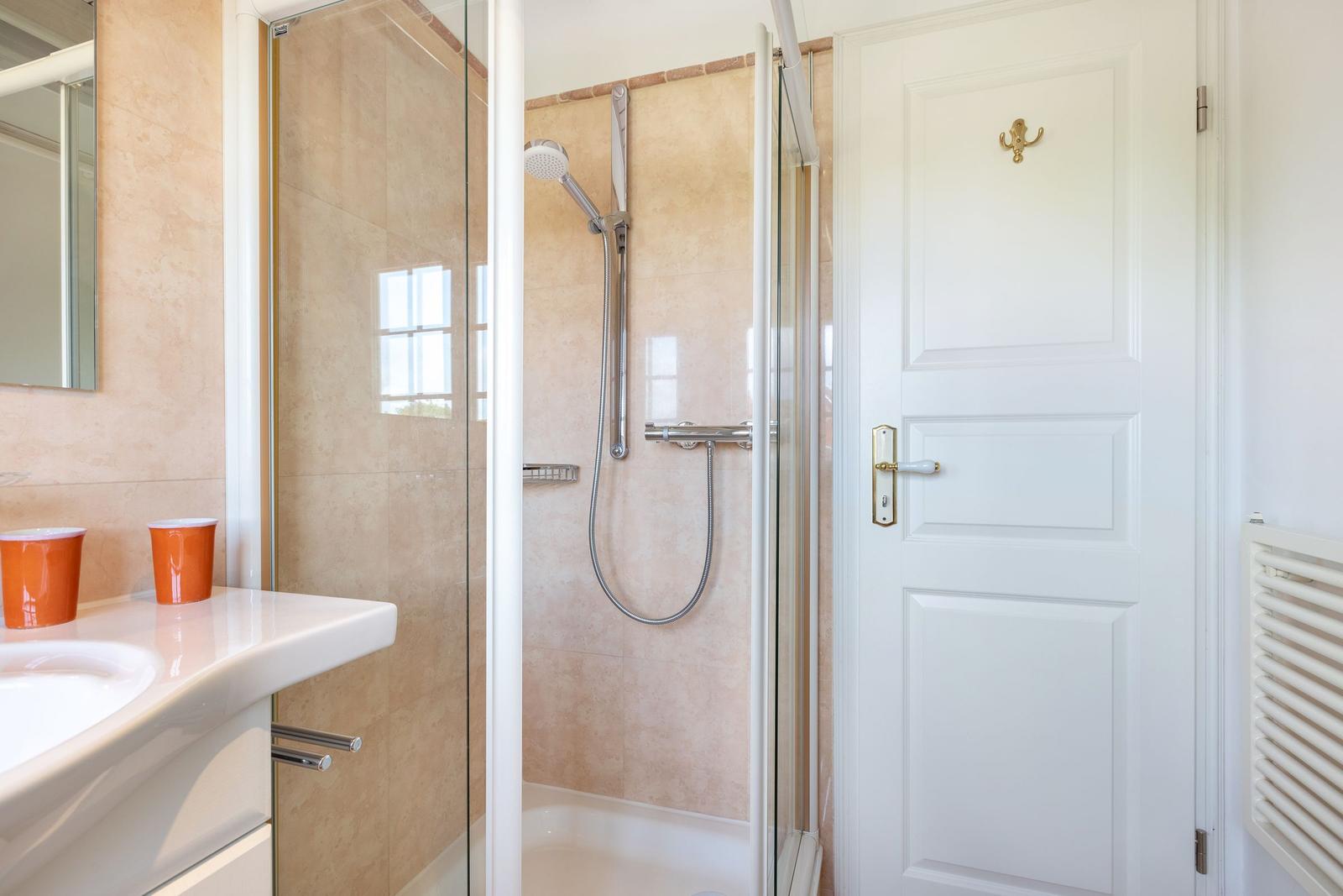 Badezimmer mit Dusche, Waschbecken und Spiegel.