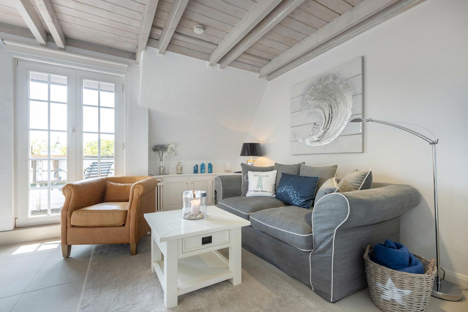 Wohnzimmer mit grauem Sofa, braunem Sessel und Holzbalkendecke.