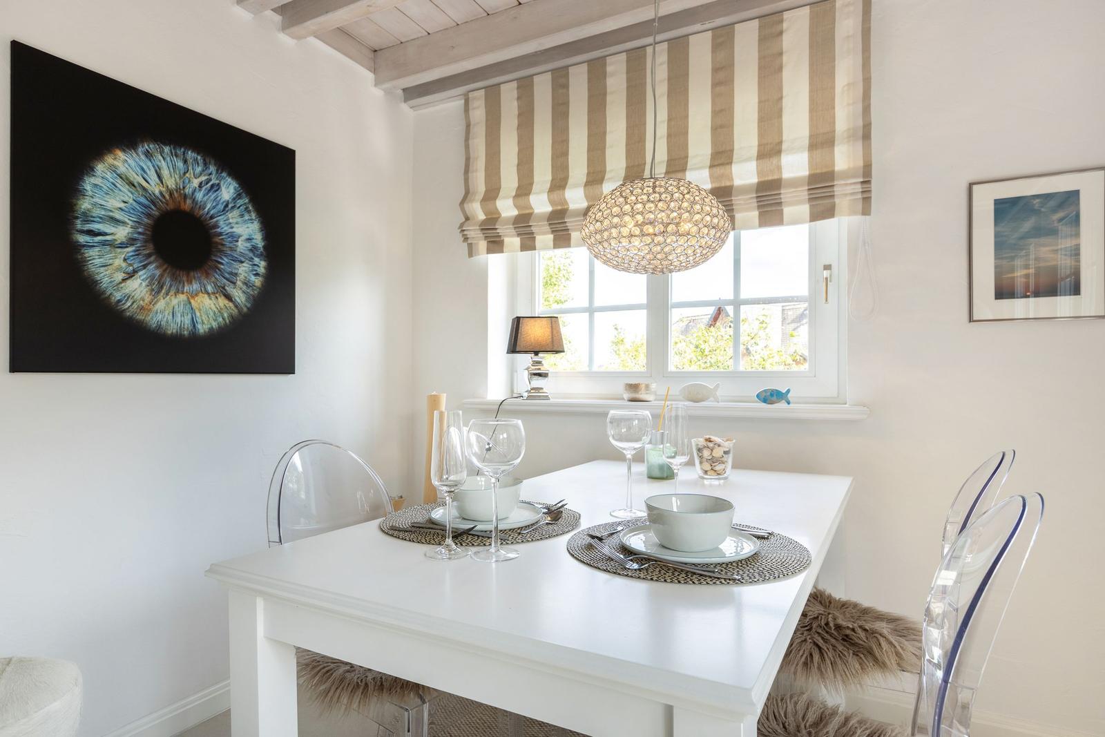 Esszimmer mit weißem Tisch, transparenten Stühlen und Wandbild eines Auges.