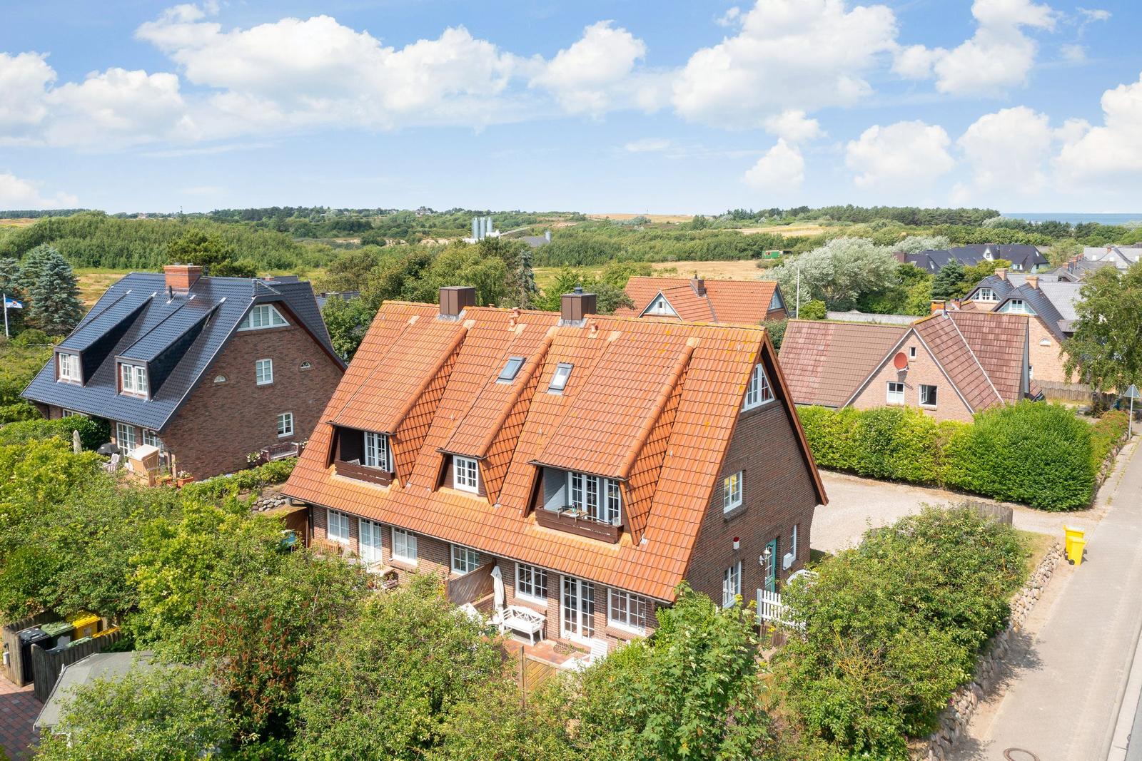 Haus mit rotem Ziegeldach und umliegenden Bäumen unter blauem Himmel.