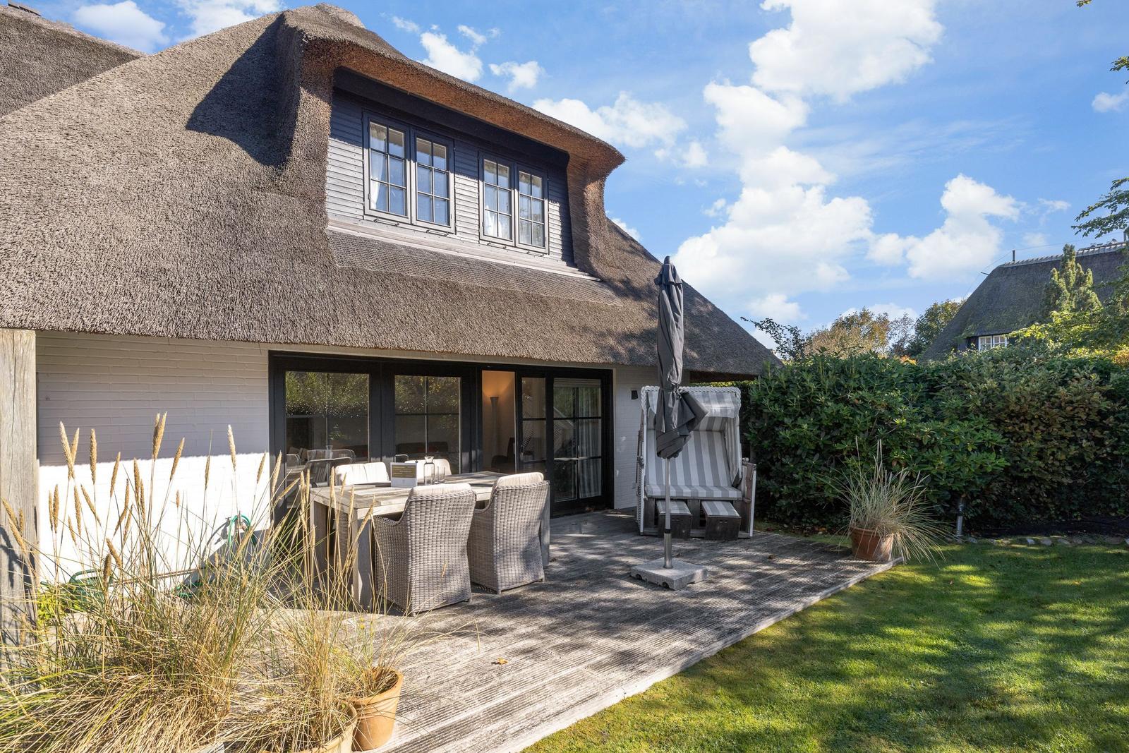 House with thatched roof, terrace with table, chairs, and lounge chair.