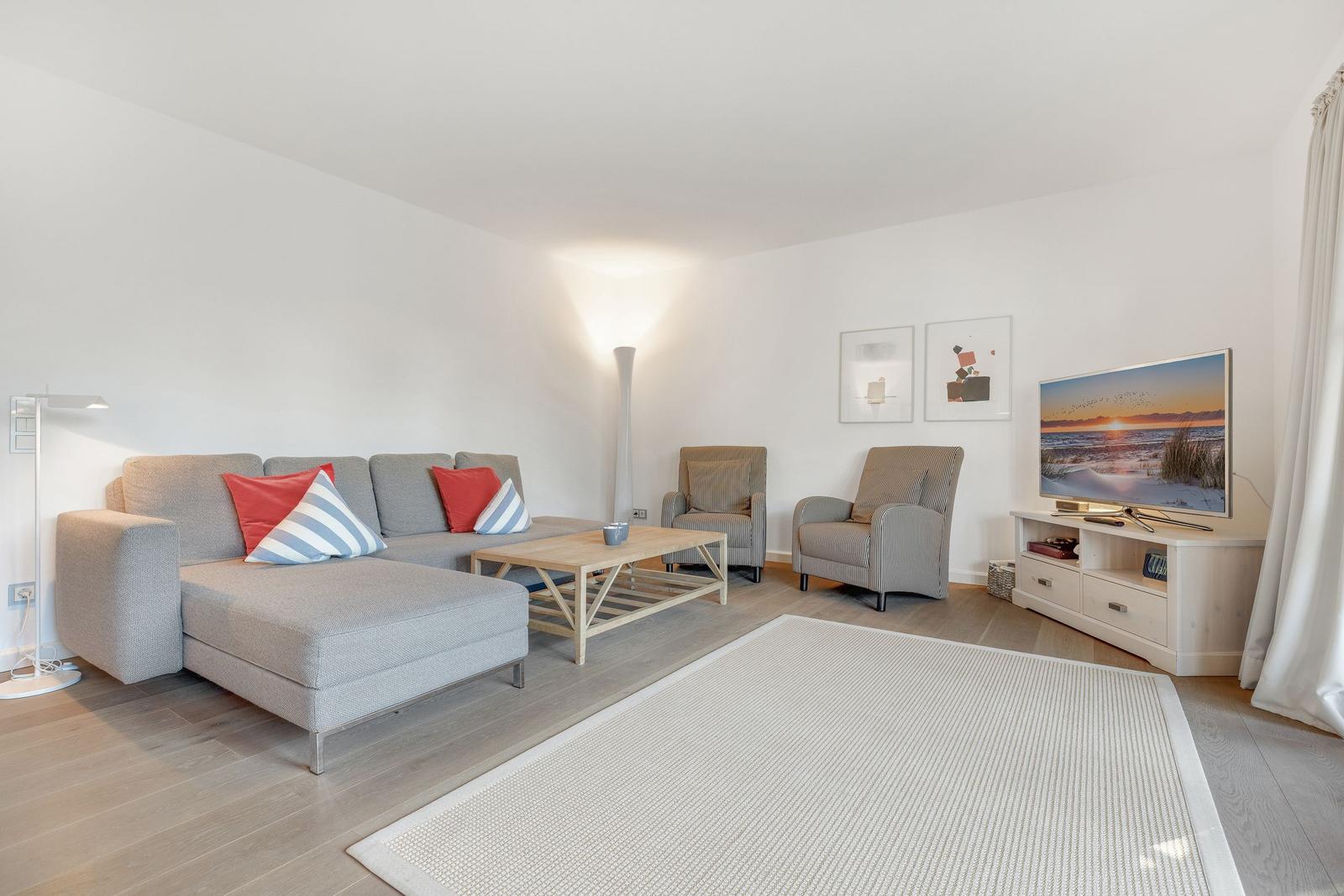 Living room with sofa, armchairs, and TV on white walls.