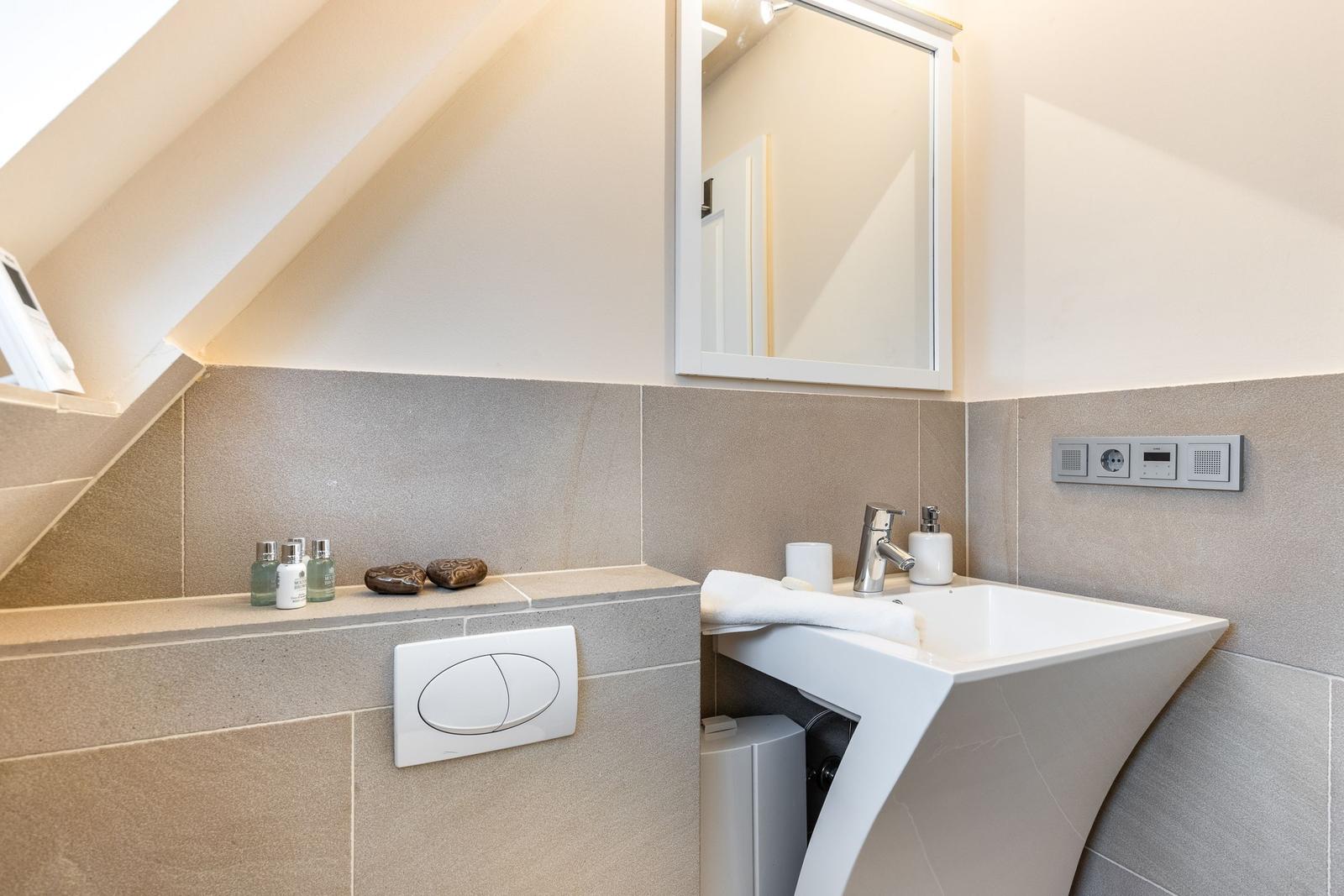 Bathroom with sink, mirror, and shower area under sloped ceiling.