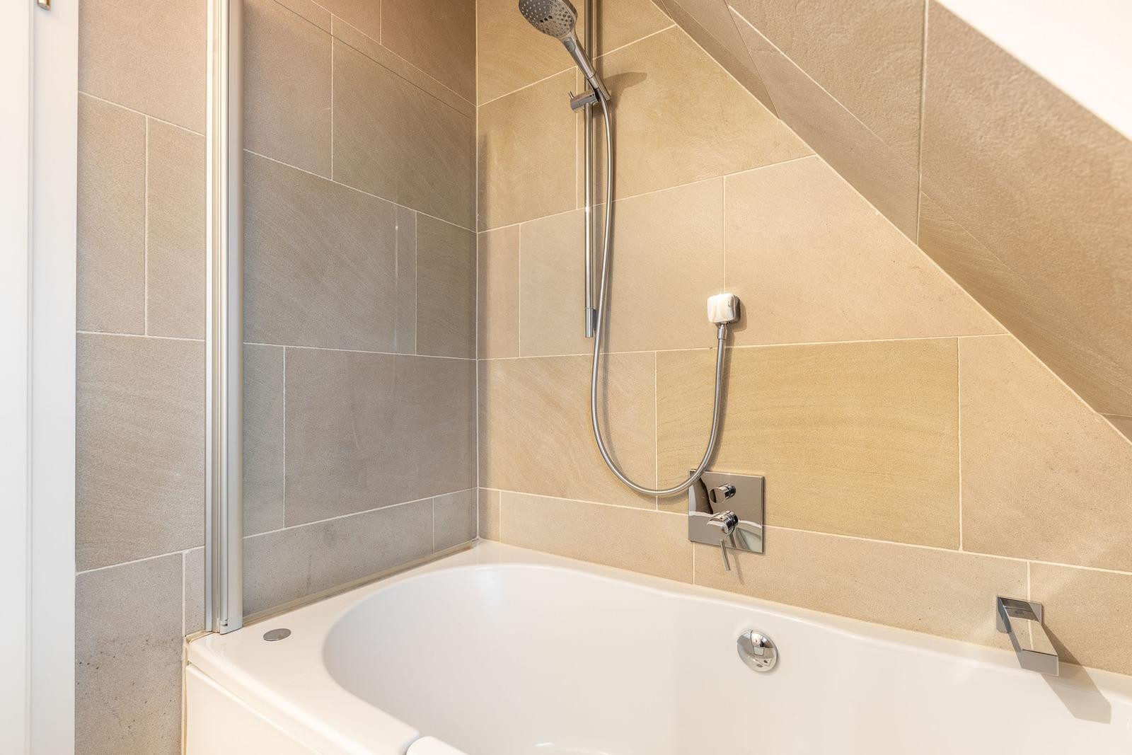 Shower with shower head and bathtub under sloped ceiling