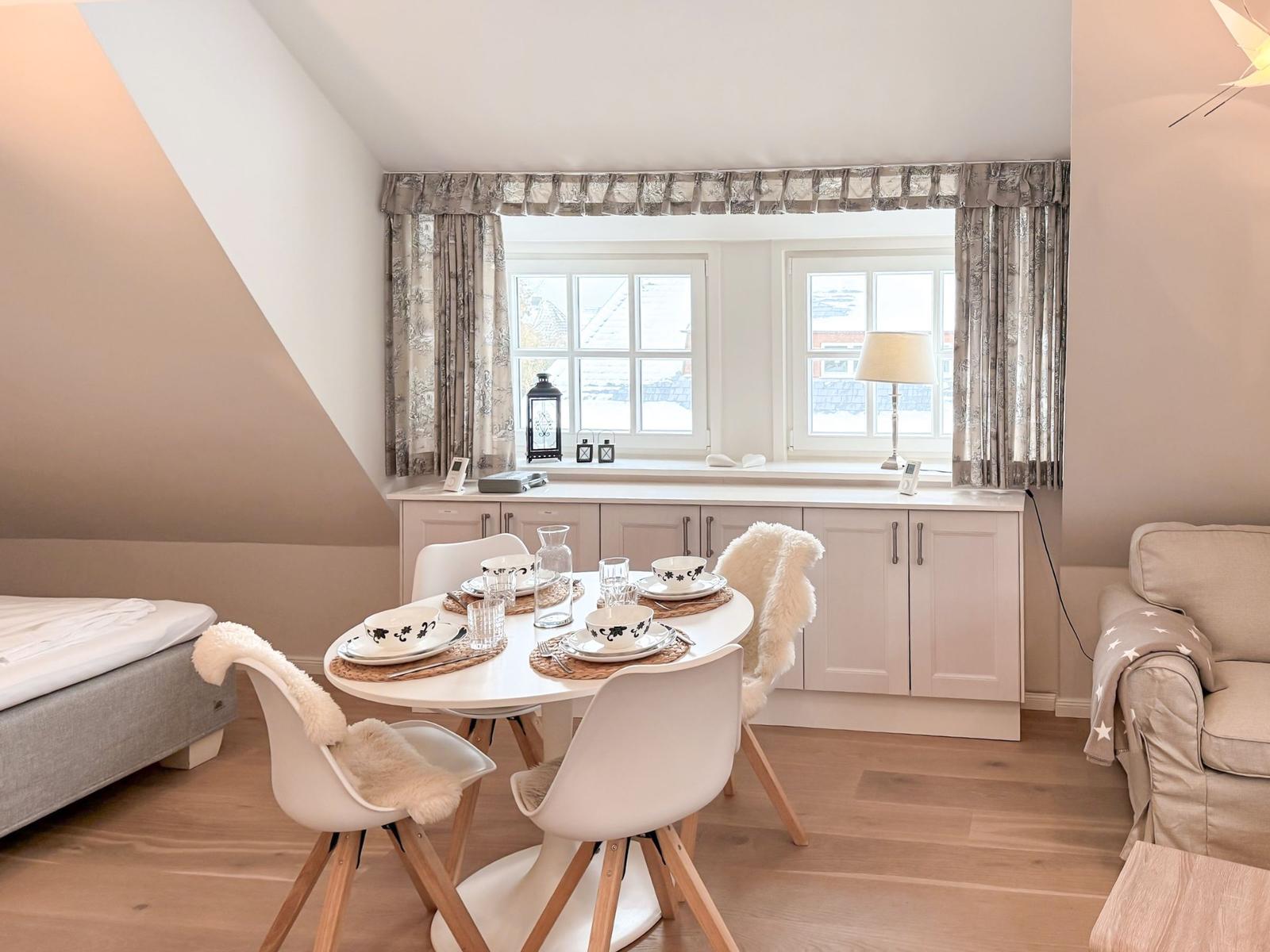Dining room with table, chairs, and windows. Adjacent room with sofa and bed.