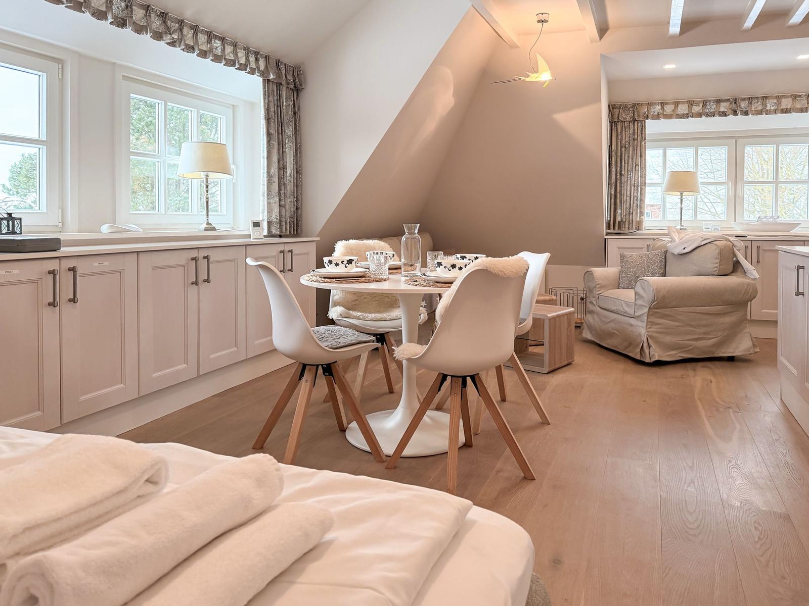 Open living and dining area with sleeping space. Wooden floor, windows, and furniture.