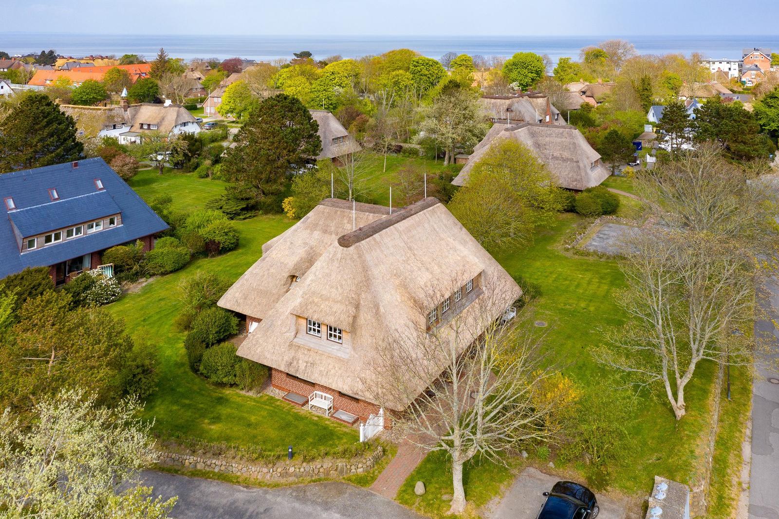 Cottage with thatched roof and green garden. View of the sea.