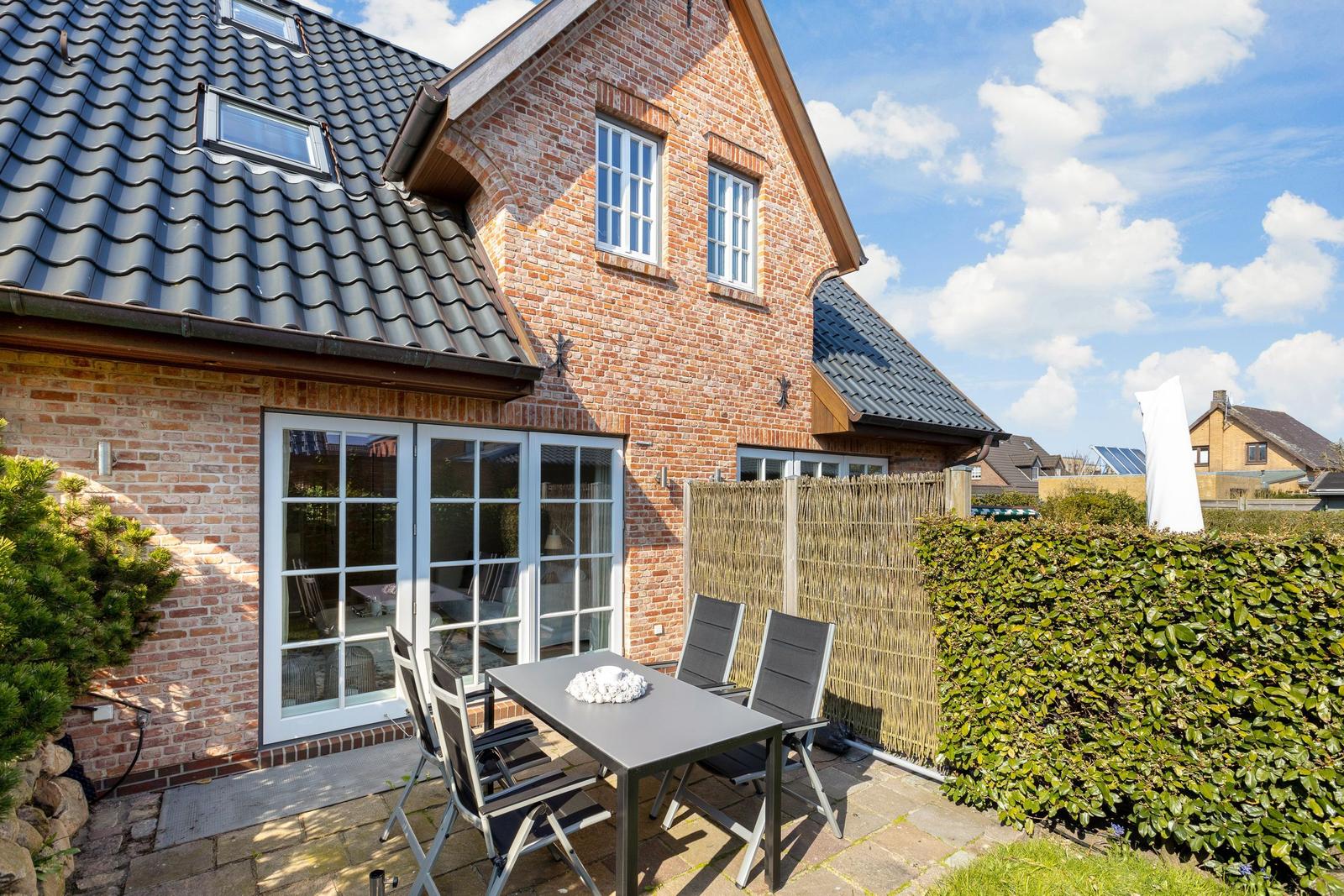 Red brick house with terrace and garden furniture under blue sky.