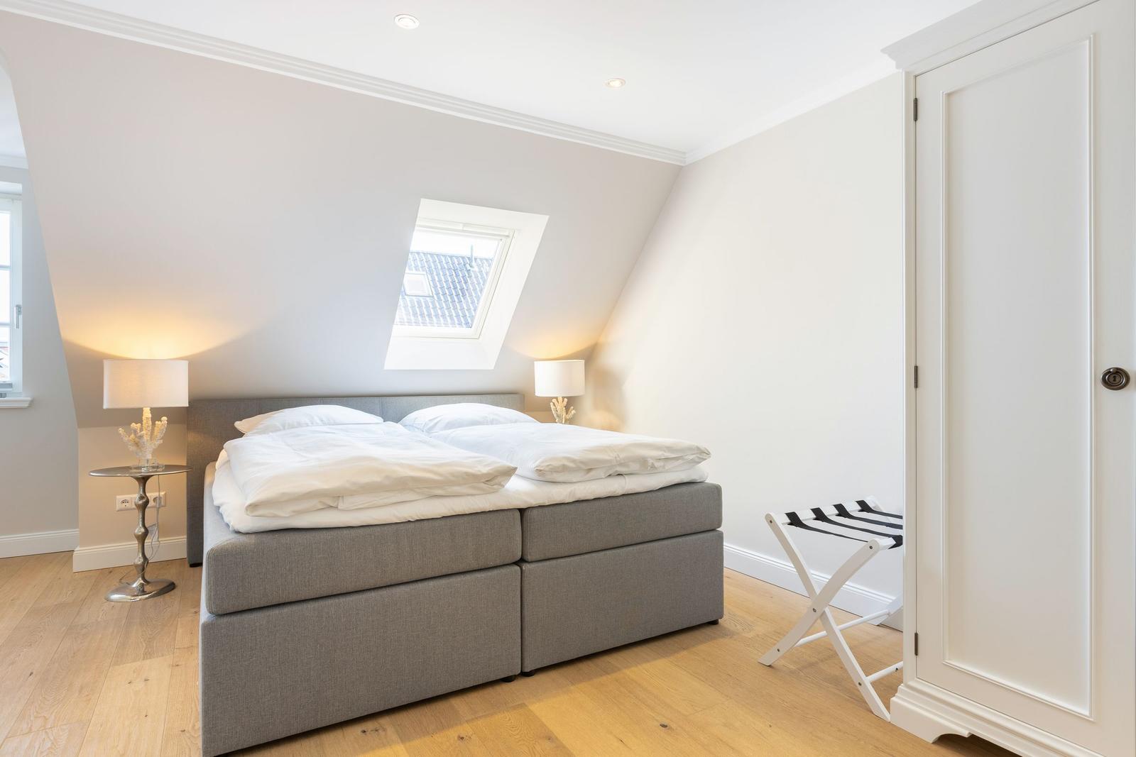 Bedroom with double bed, sloped ceiling, skylight, and wooden floor.