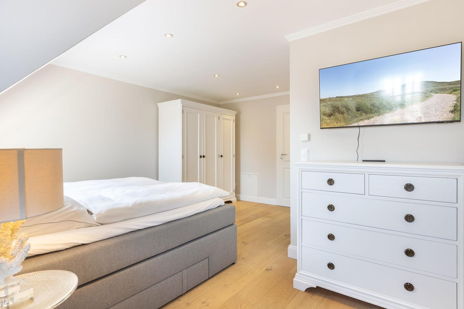 Bedroom with bed, wardrobe, and TV. Wooden floor and white furniture.