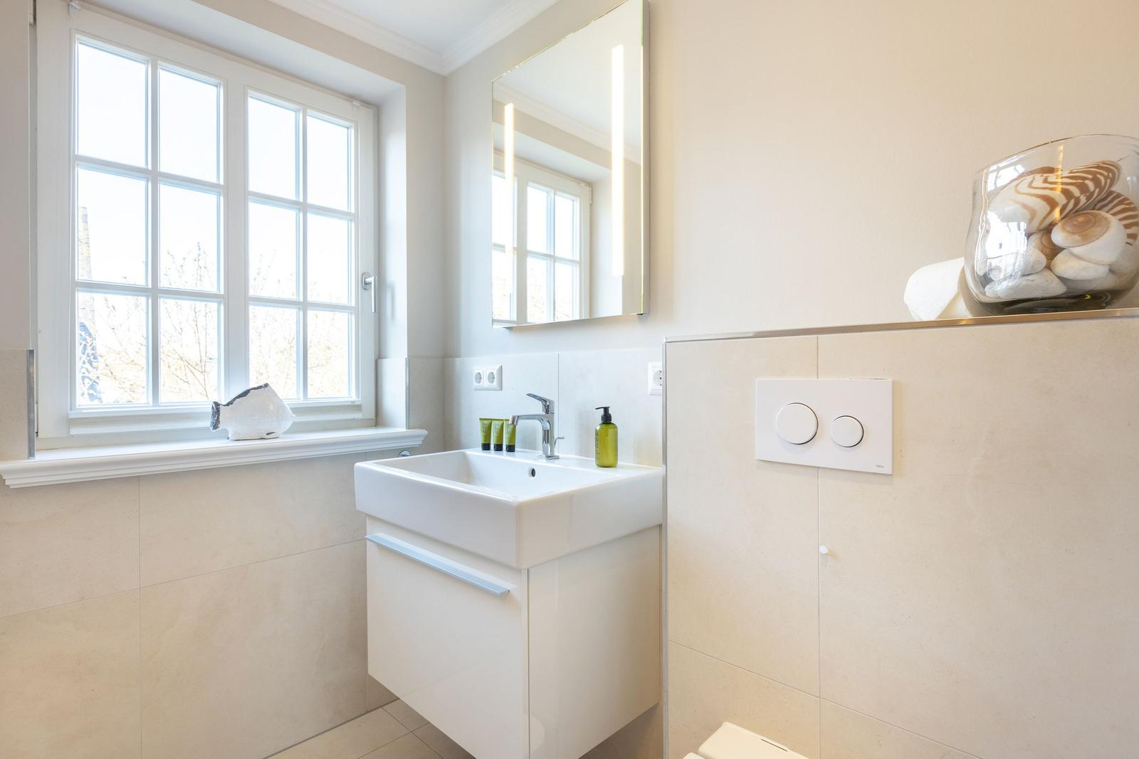Bathroom with sink, mirror, and window. A bowl with stones sits on the windowsill.