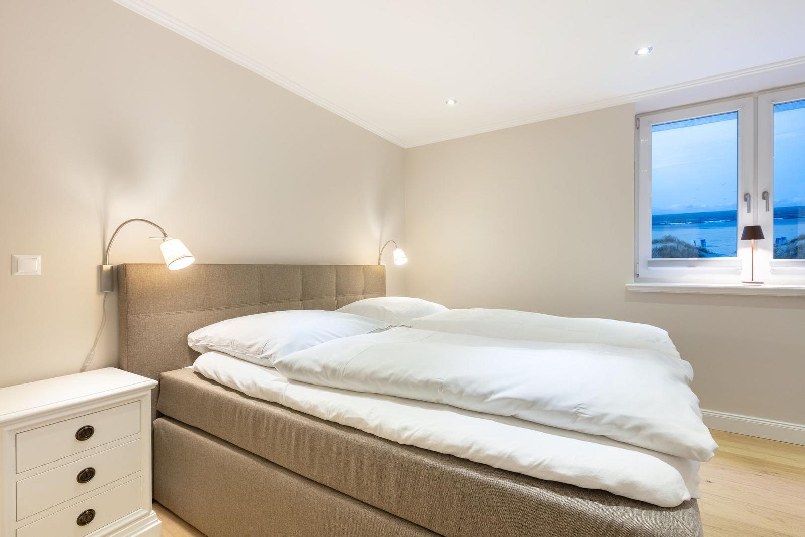 Bedroom with bed, nightstand, and sea view through window.