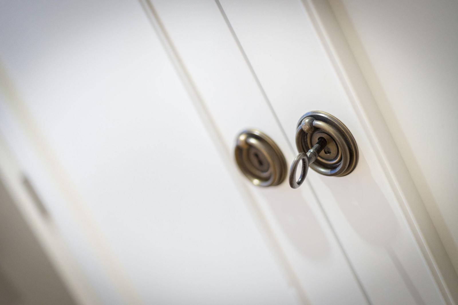 Key in the lock of a white door with metallic handles.