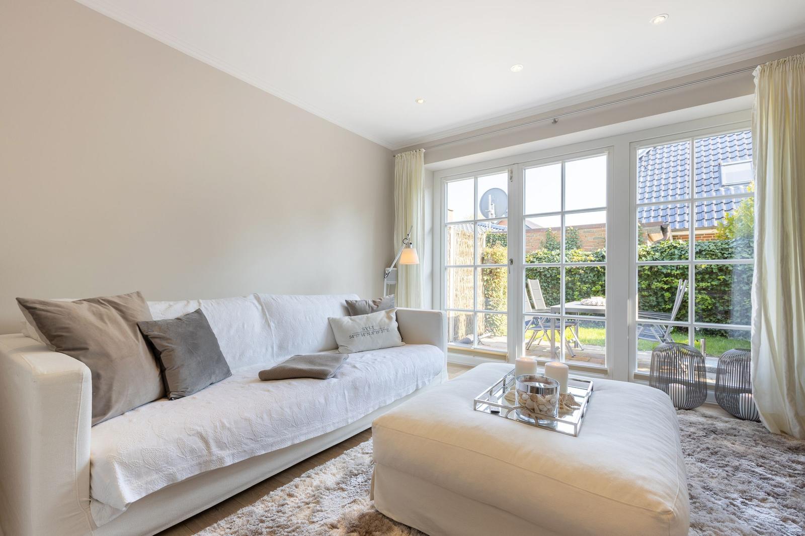 Living room with white sofa, ottoman, and view of the garden.