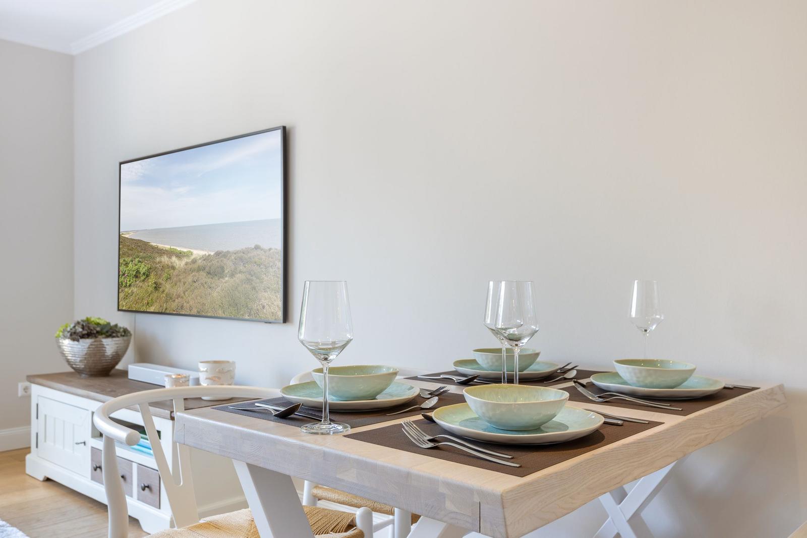 Dining table with four place settings, wall art, and sideboard in dining room.