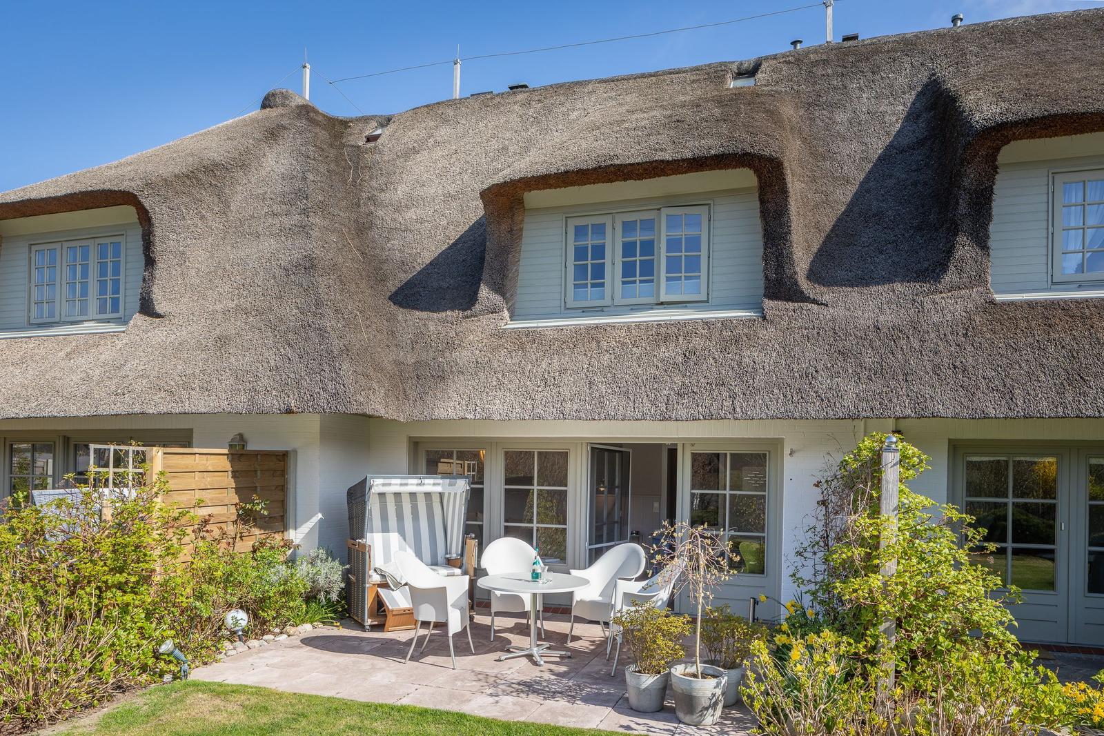 Haus mit Strohdach, Terrasse mit Tisch und Stühlen, Gartenbereich mit Pflanzen.