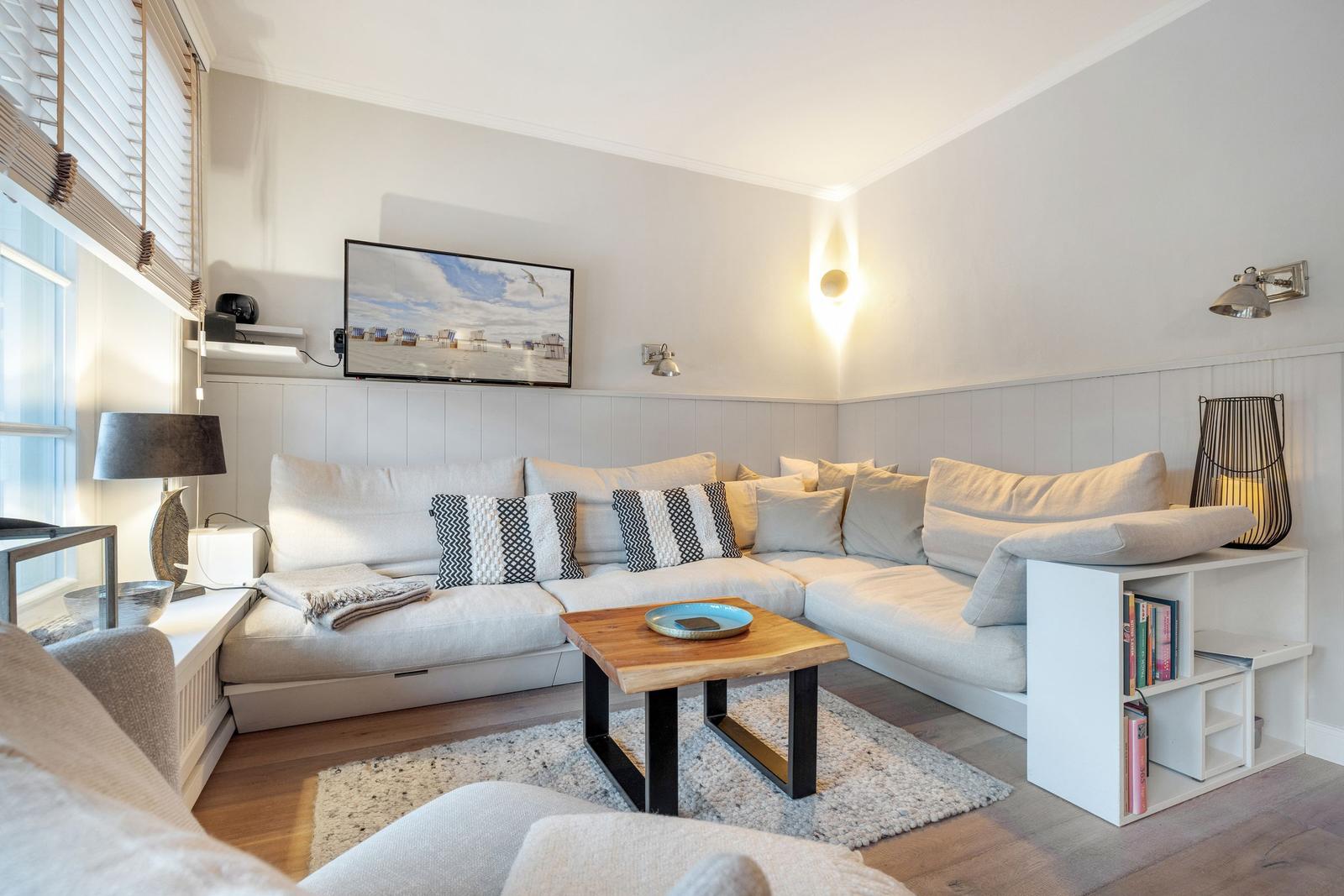 Wohnzimmer mit Ecksofa, Fernseher und Holztisch auf Teppich.