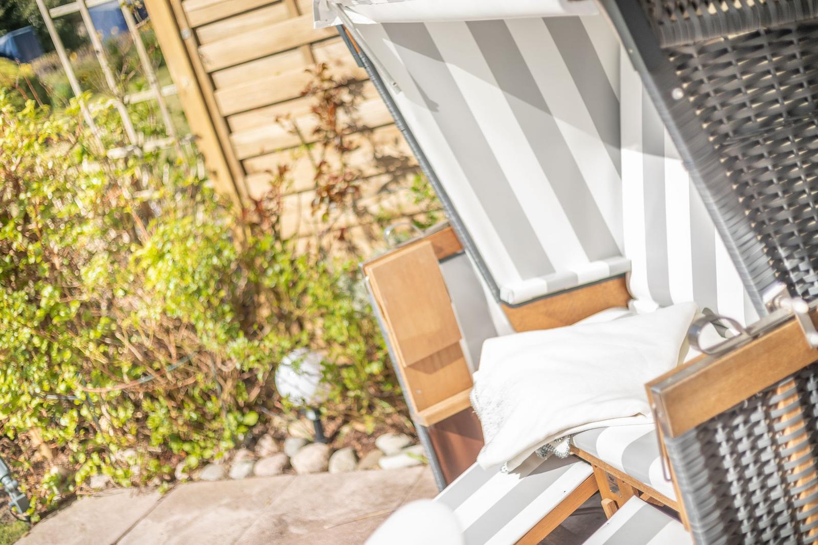 Liegestuhl mit Streifen auf Terrasse neben grüner Hecke.
