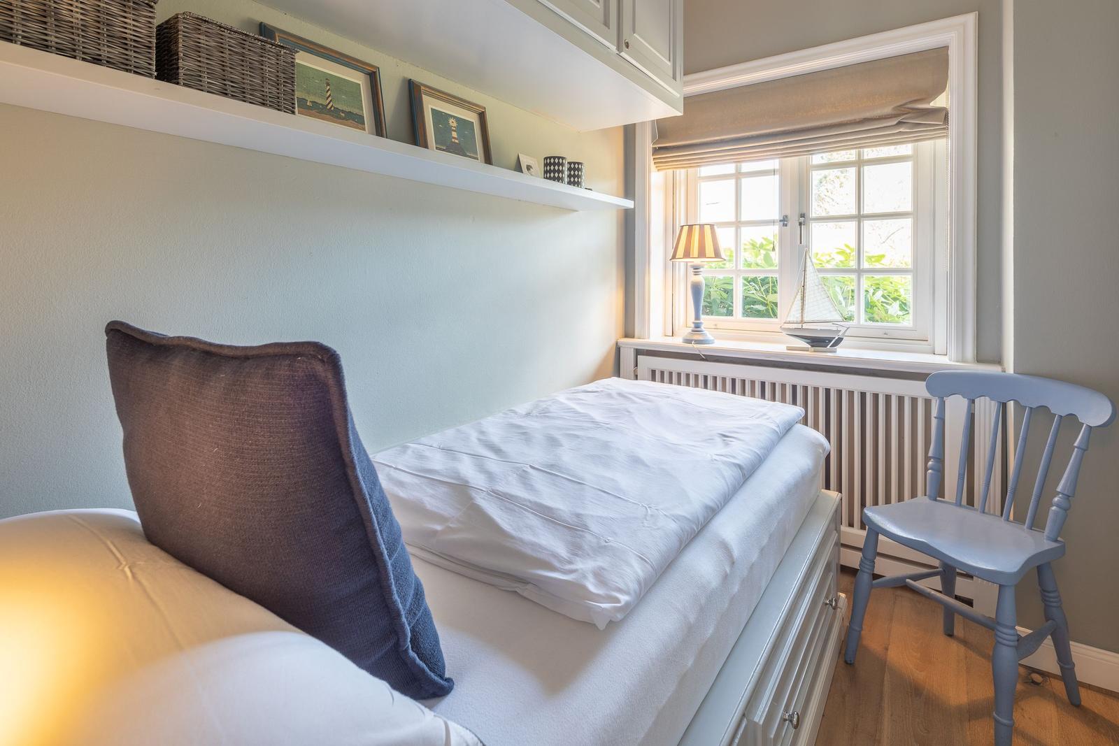 Schlafzimmer mit Bett, Stuhl und Fenster mit Blick auf Grün.