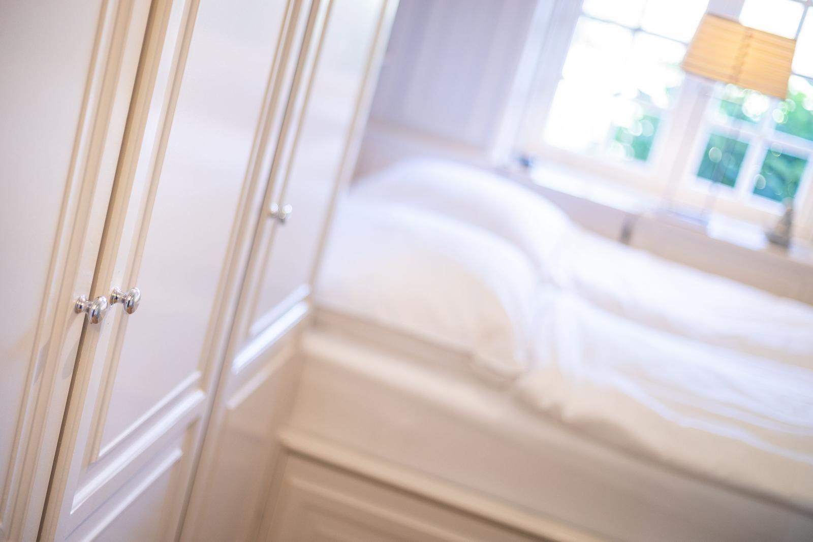Schlafzimmer mit weißem Bett und Kleiderschrank mit silbernen Knöpfen.