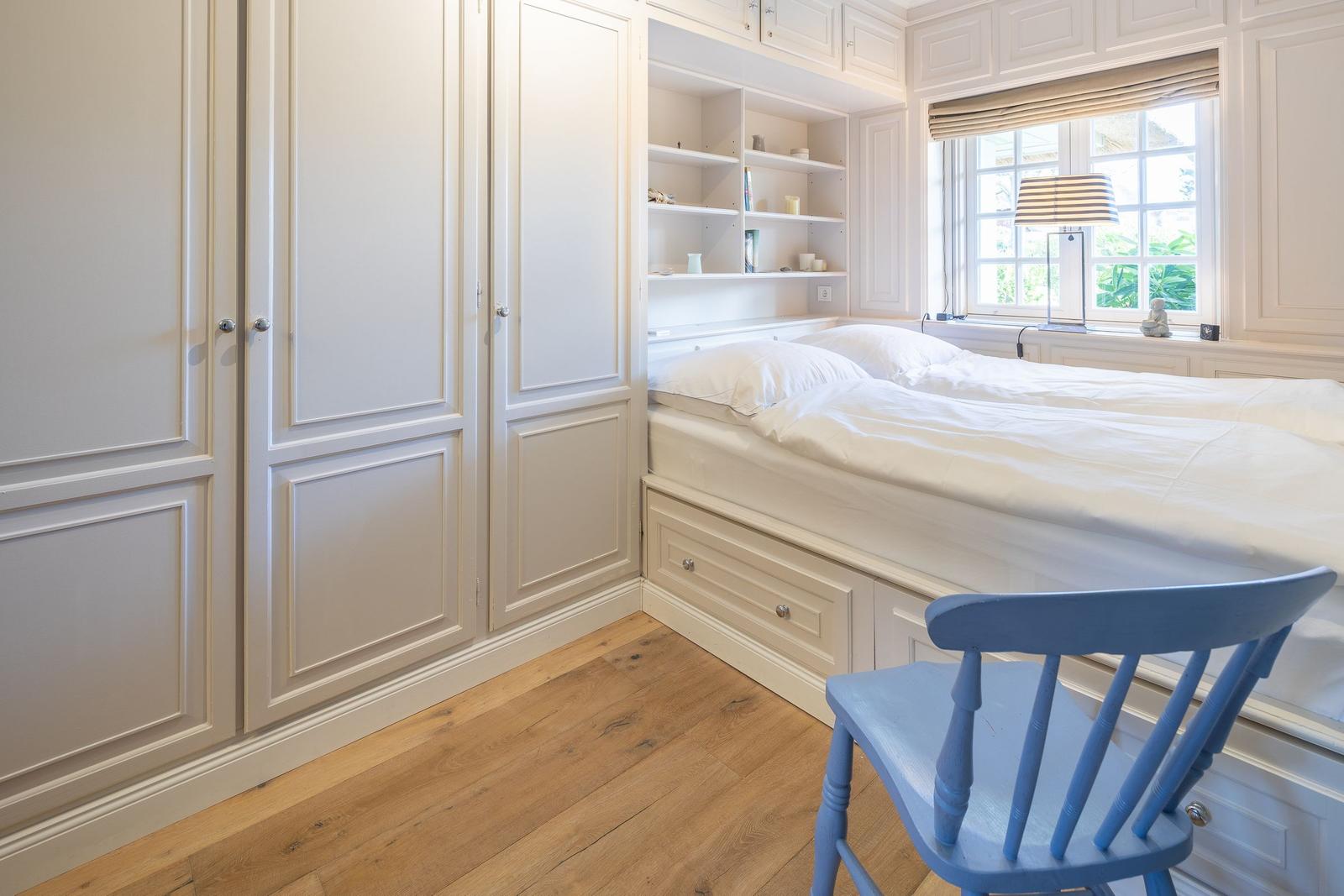 Schlafzimmer mit weißem Bett, Kleiderschrank und blauer Stuhl.