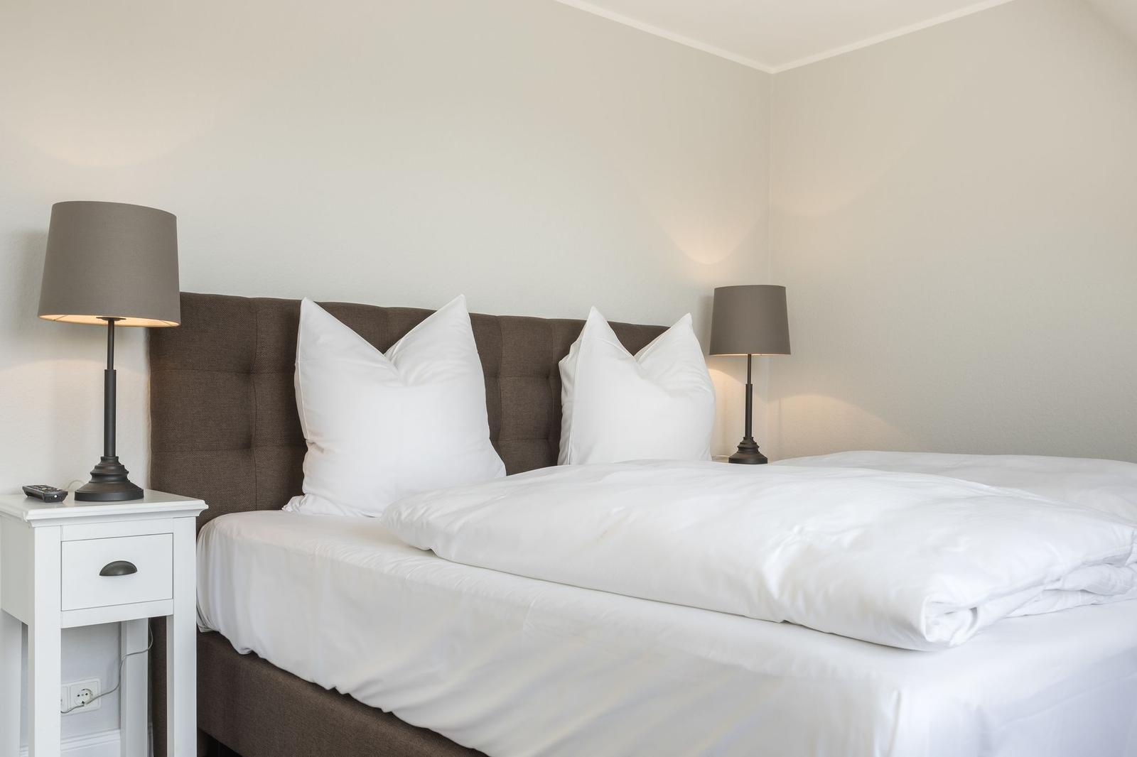 Schlafzimmer mit Bett, weißen Laken und zwei Nachttischen mit Lampen.