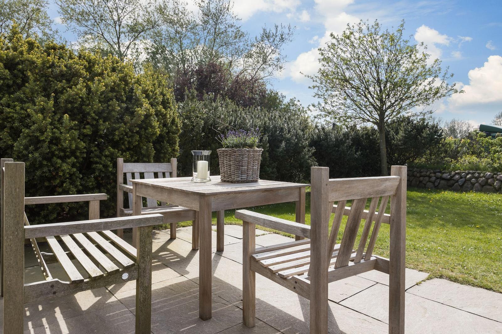 Holztisch mit Stühlen auf Terrasse, Pflanze und Kerze im Hintergrund.