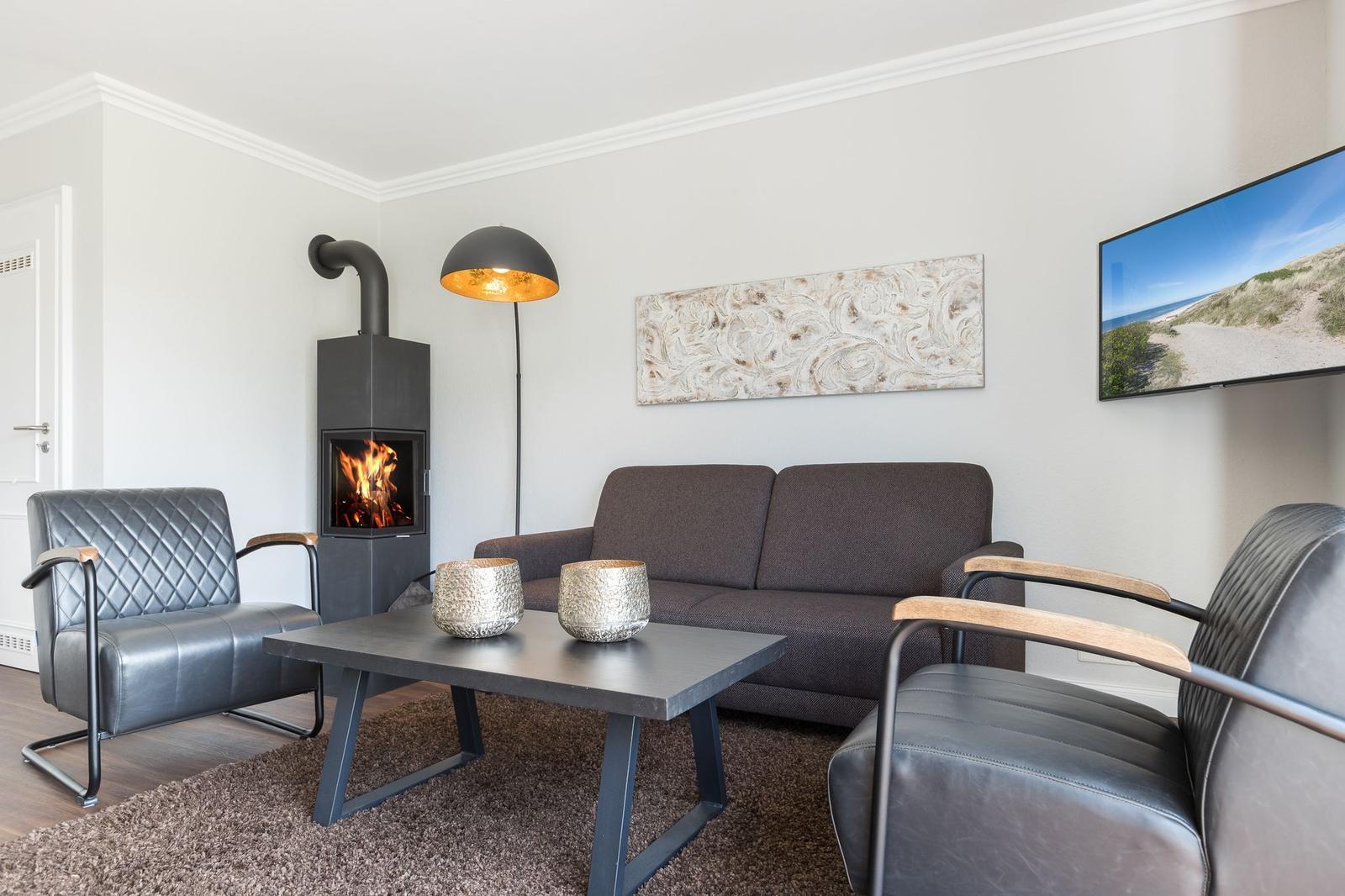 Wohnzimmer mit Sofa, zwei Sesseln, Kamin und Fernseher an der Wand.