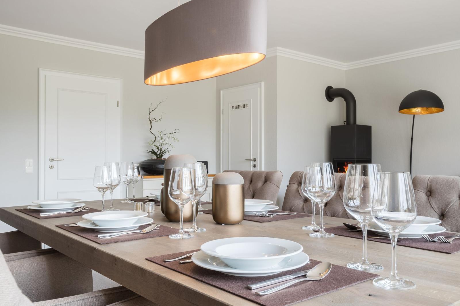 Esstisch mit Platz für sechs Personen, moderne Beleuchtung und Kamin im Hintergrund.