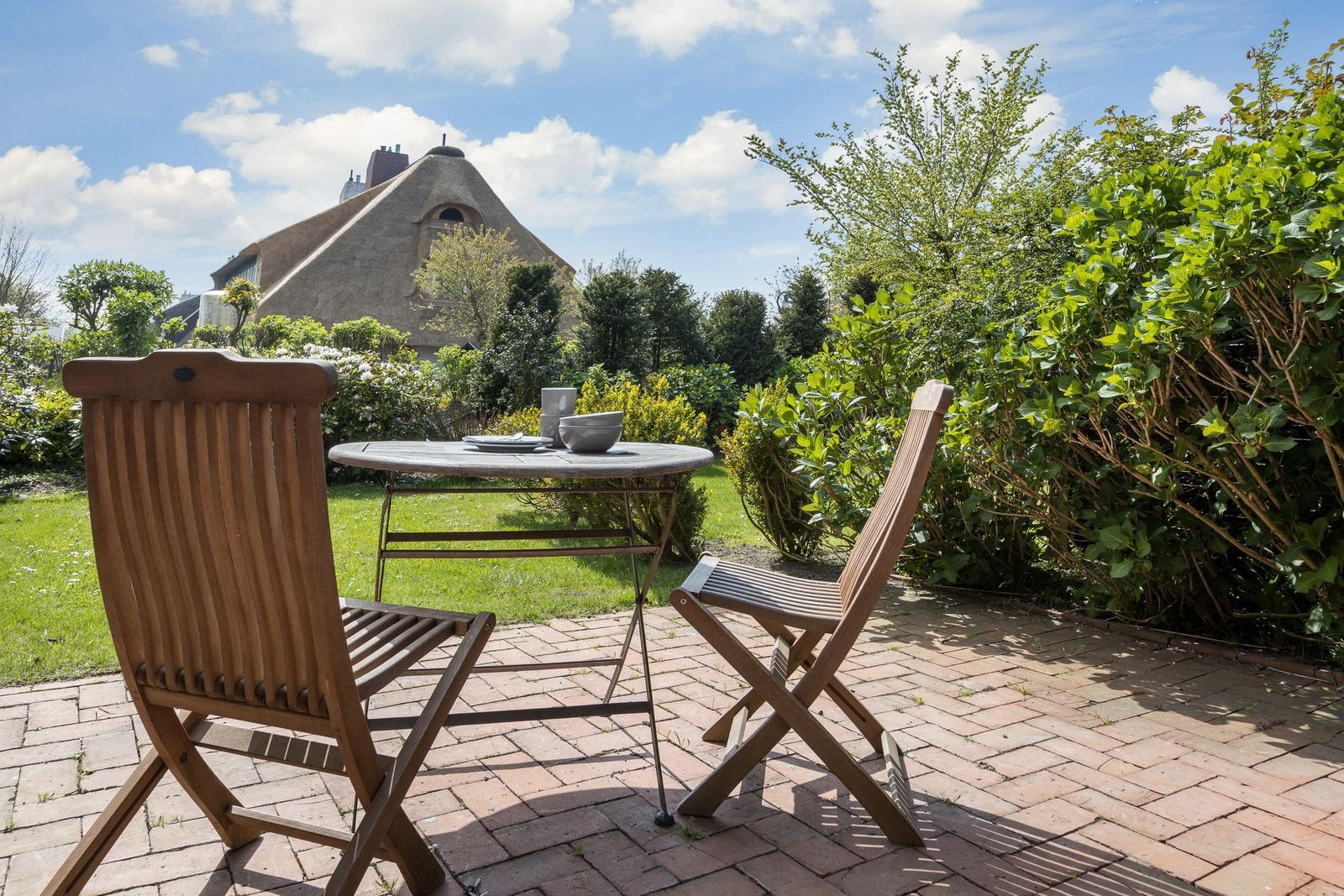 Hinterhof mit Tisch und zwei Stühlen. Im Hintergrund ein traditionelles Haus mit Strohdach.