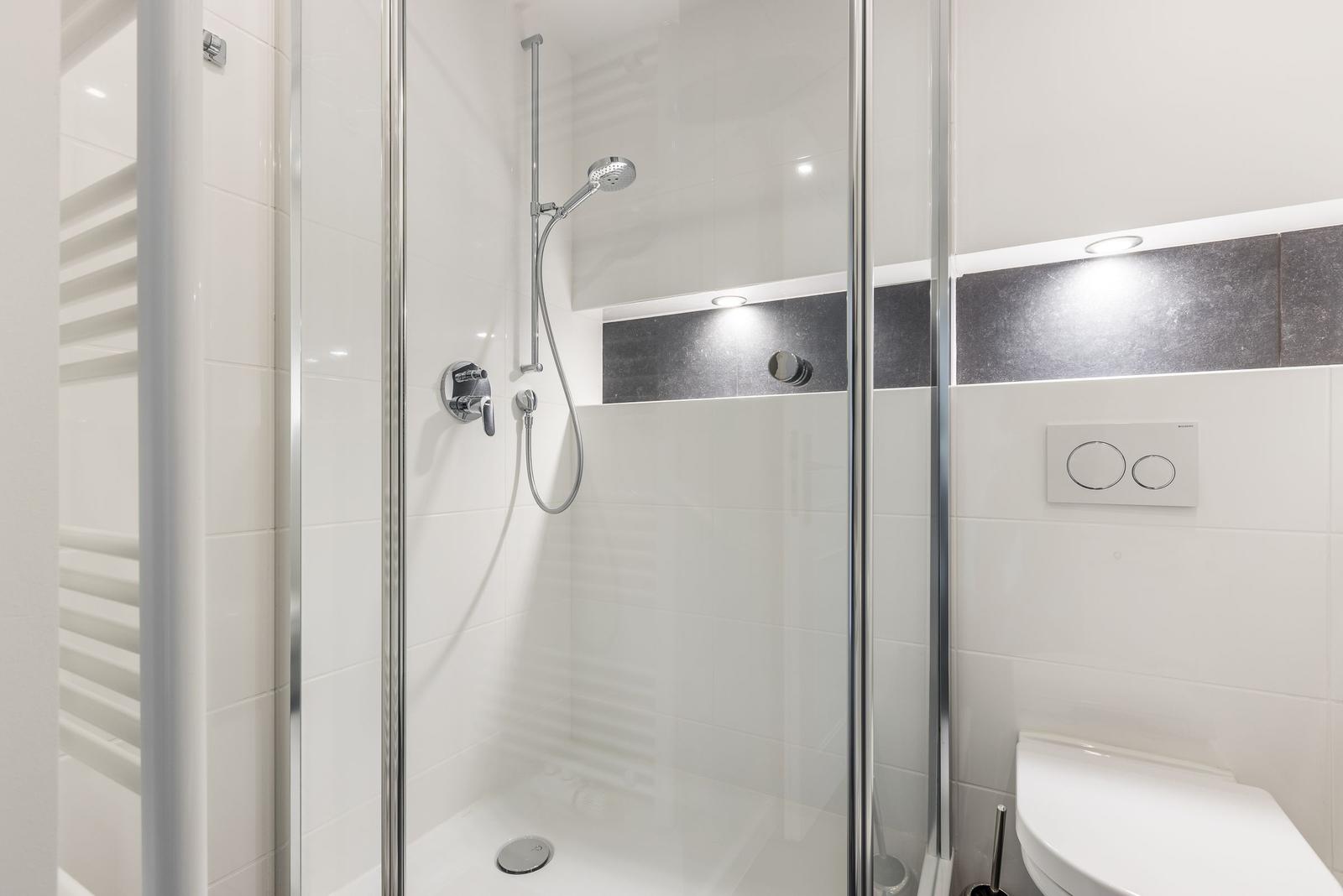 Duschkabine mit Duschbrause, Toilette und Heizkörper.