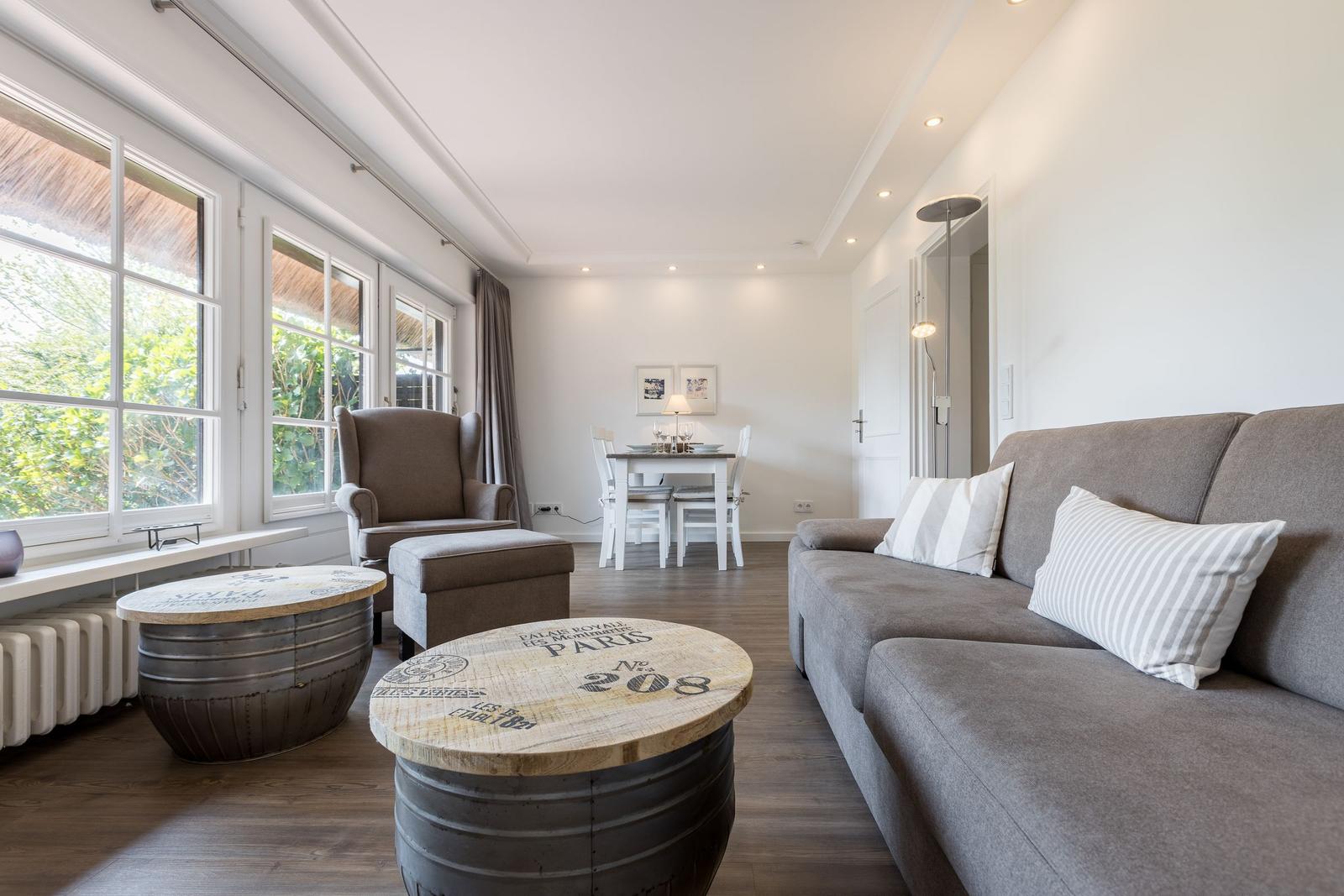 Wohnzimmer mit Sofa, Sitzgruppe und Essbereich. Fenster mit Blick auf Garten.