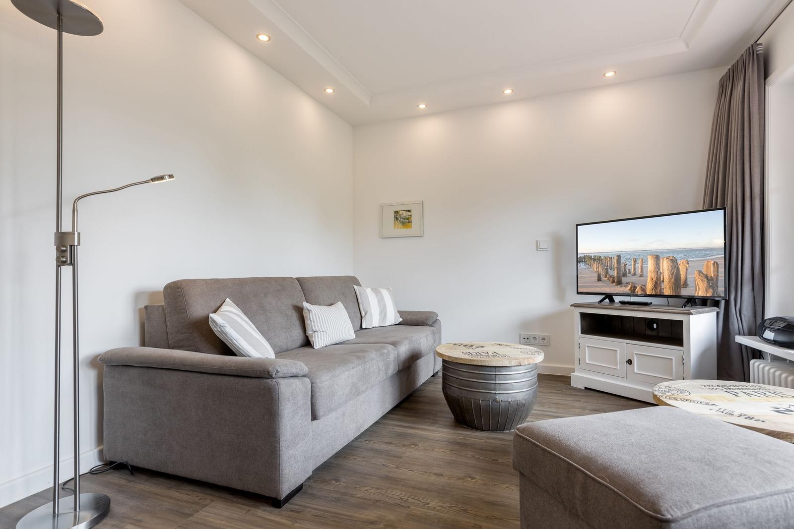 Wohnzimmer mit Sofa, Fernseher und Stehlampe.