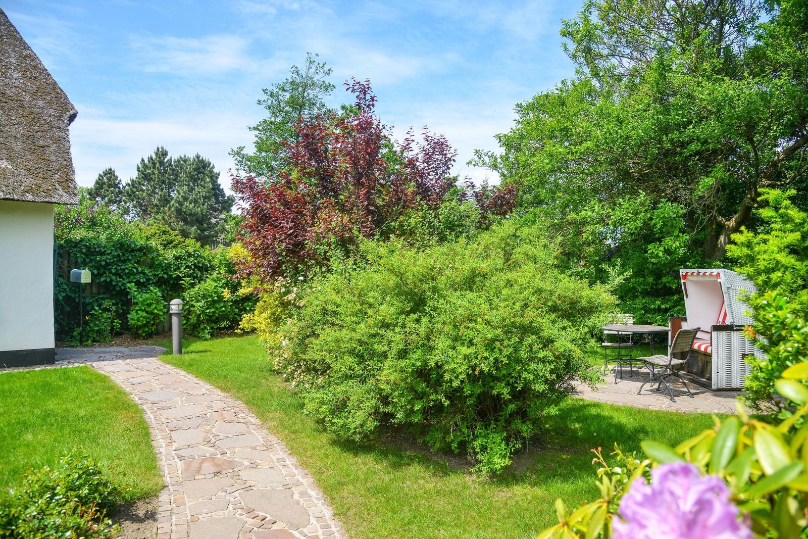Garden with stone path, flowerbeds, and beach chair. House with thatched roof.