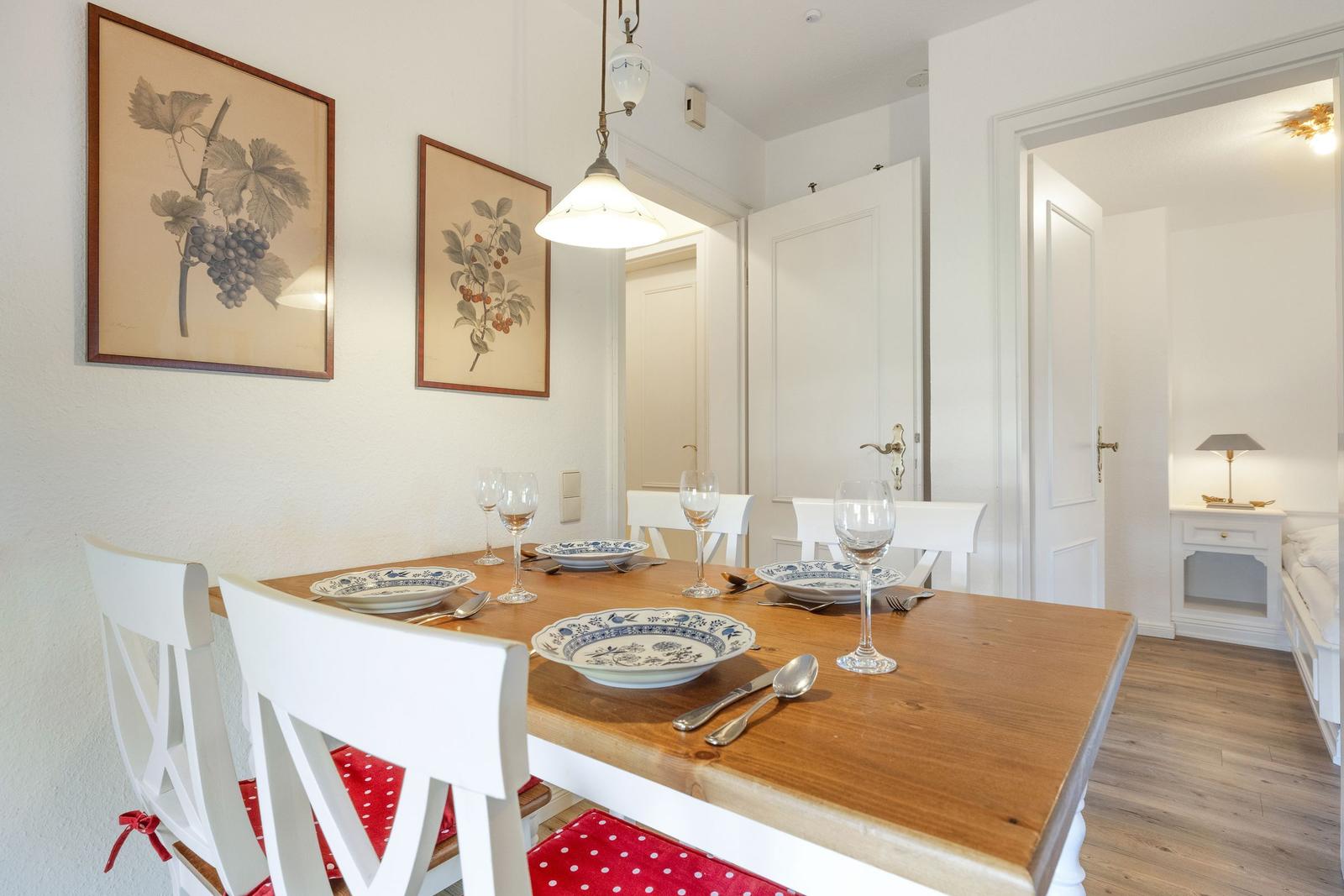 Dining room with wooden table, white chairs, and paintings on the wall.