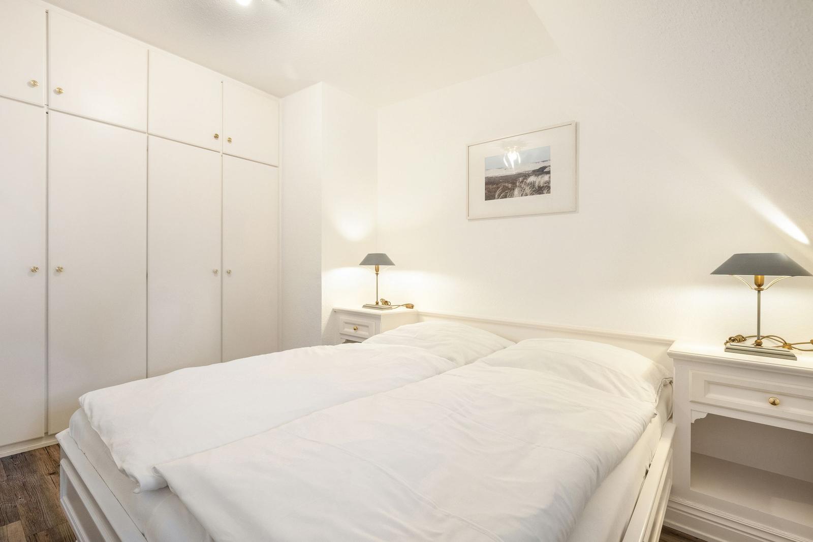 Bedroom with white bed, nightstands, and wardrobe.