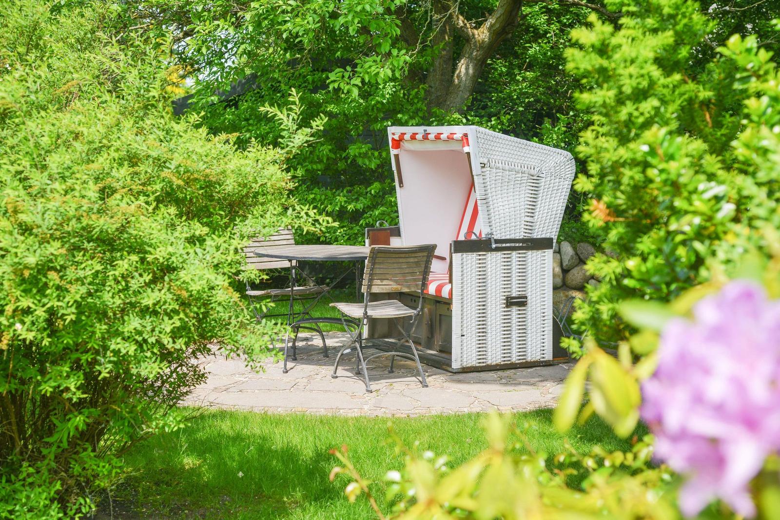 Garden with beach chair, table and chairs surrounded by green bushes.