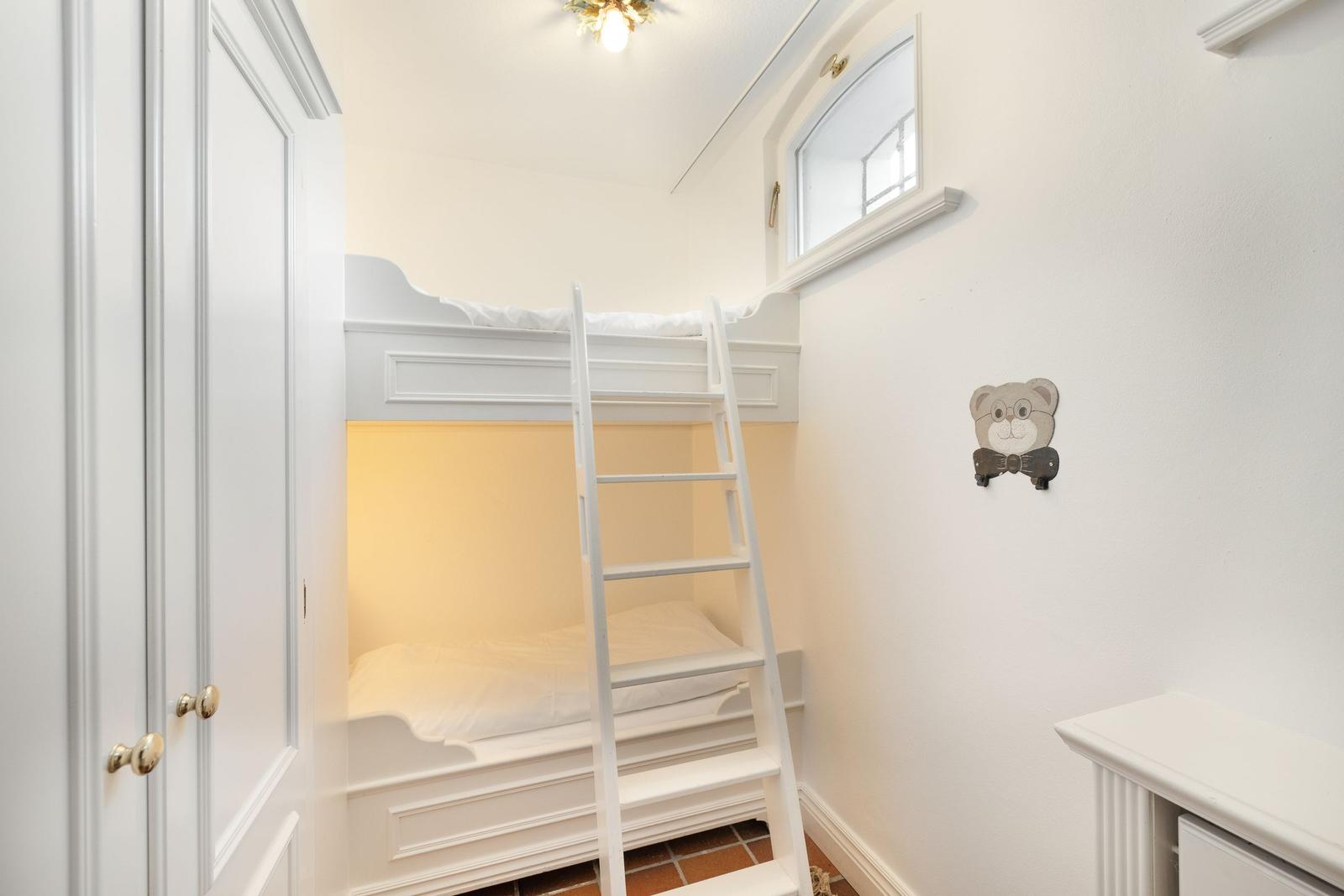 A bedroom with a bunk bed, white walls, and a small window.