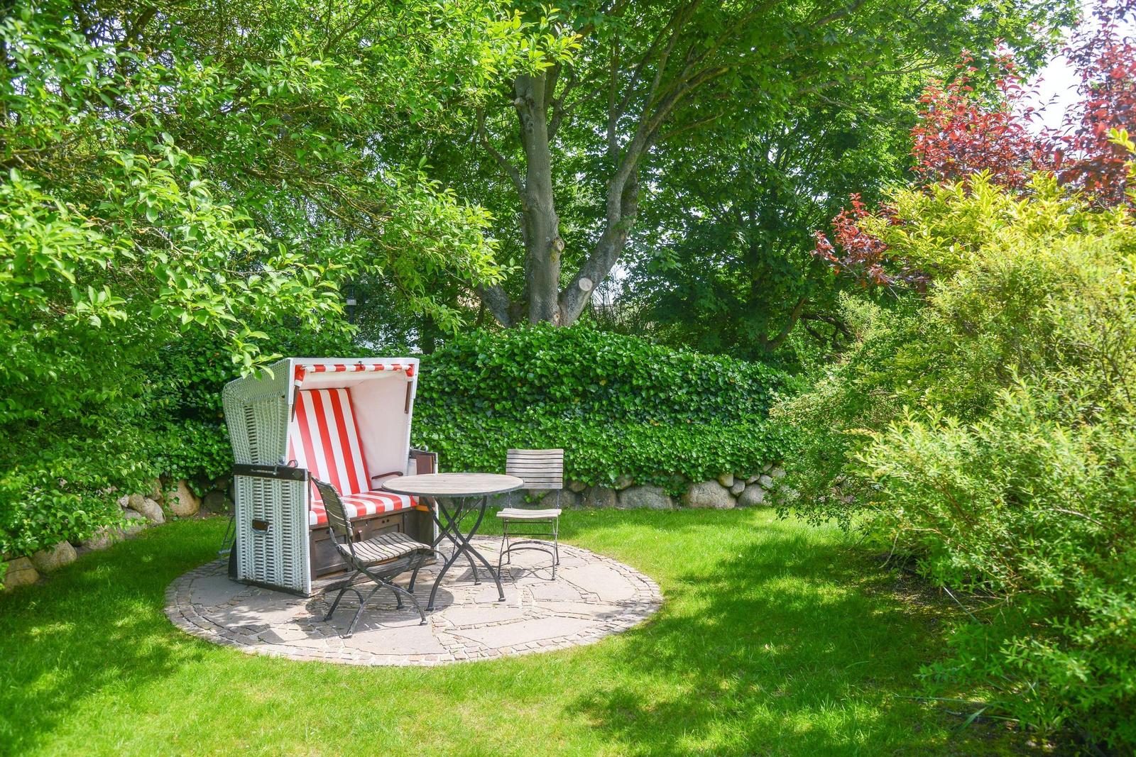 Circular stone patio with beach chair, table, and chairs in the green garden.