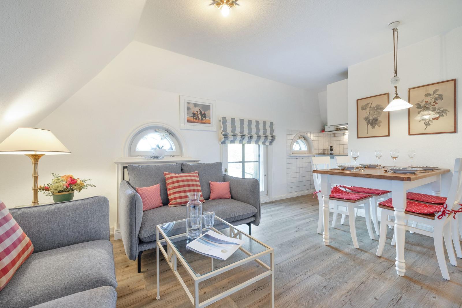 Living and dining area with sofa, table and chairs. Wooden floor and white walls.