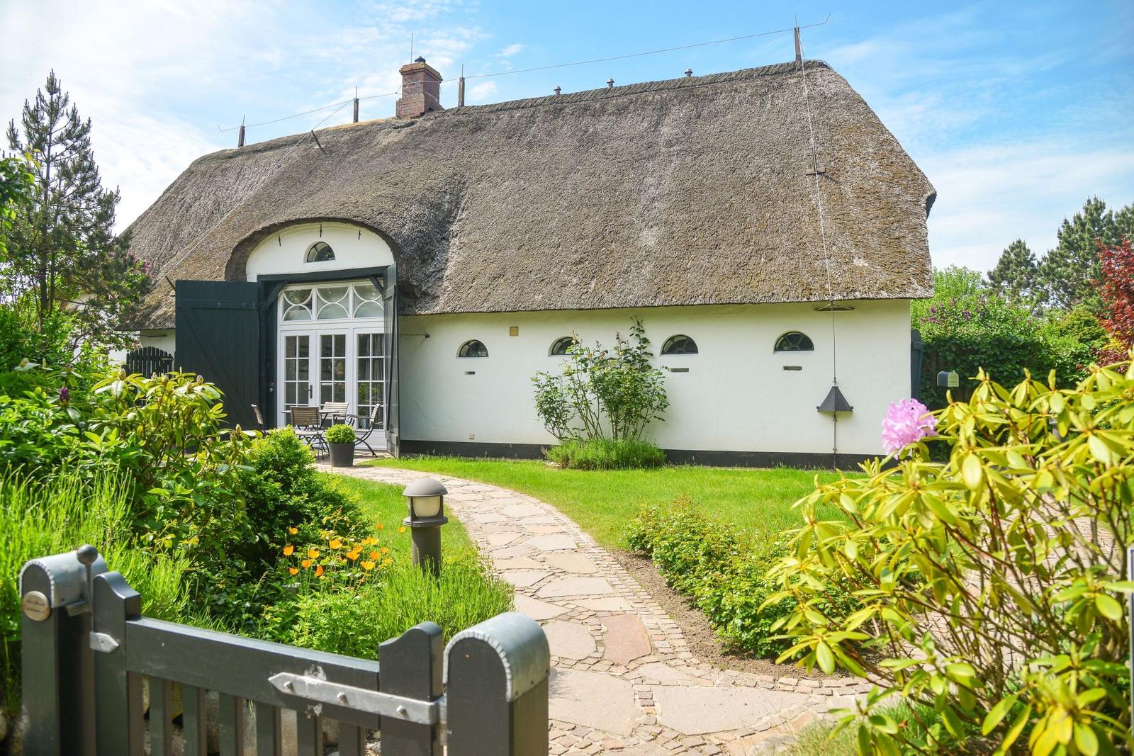 House with thatched roof, garden path, and flower beds.