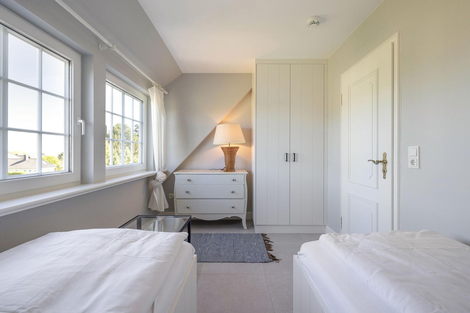 Zimmer mit zwei Betten, Schrank, Nachttisch und Fenstern.