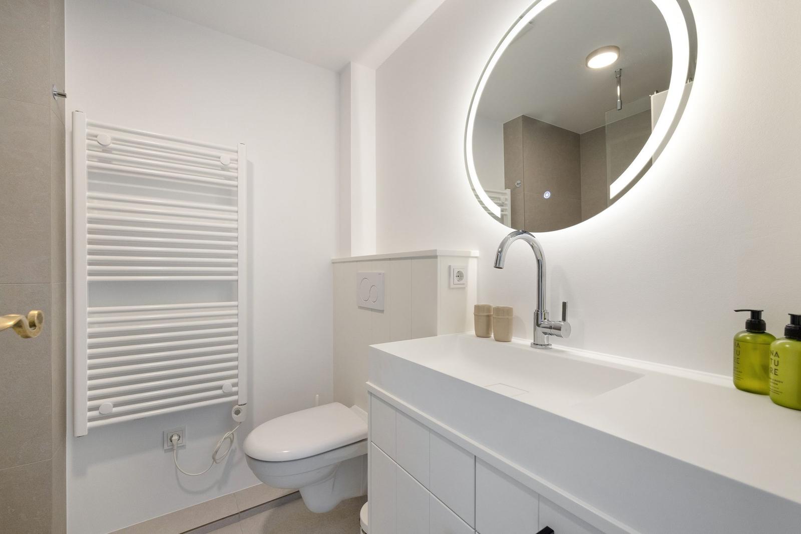 Badezimmer mit Waschtisch, Spiegel und Toilette.