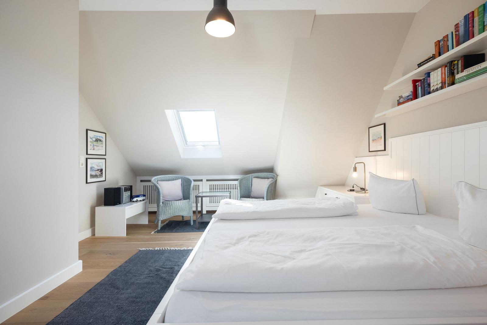 Schlafzimmer mit Dachschrägen, Bett, Sitzgelegenheit und Bücherregal.