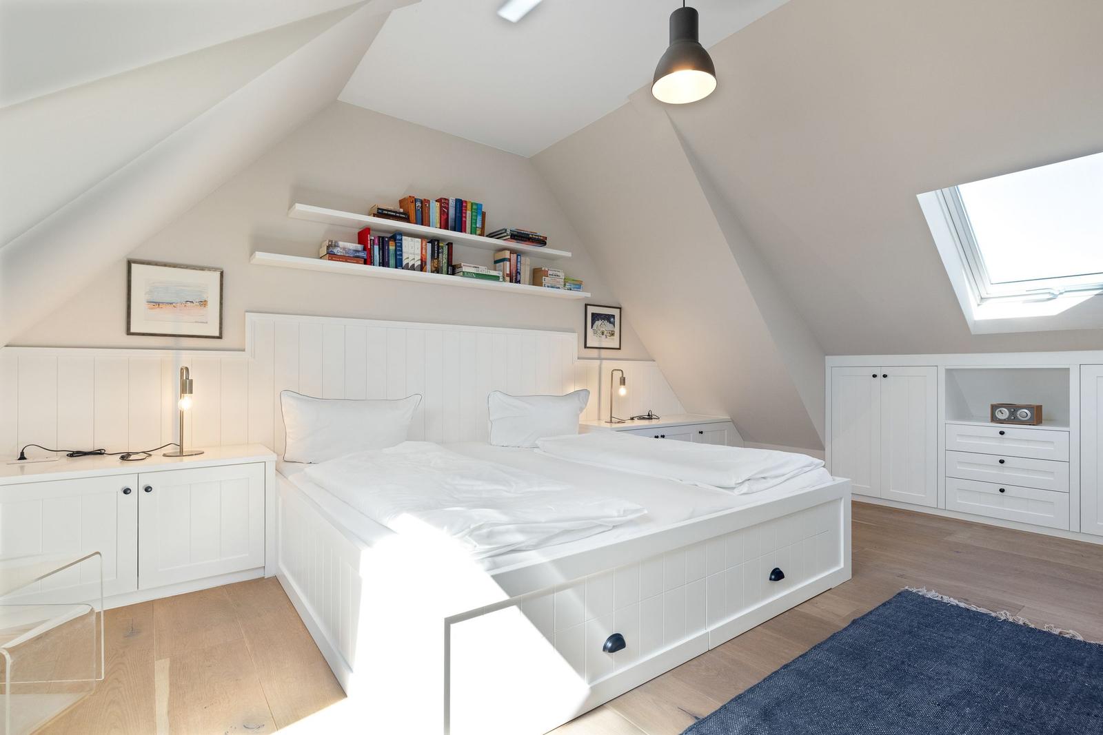 Schlafzimmer mit Dachschrägen, weißem Bett und Bücherregal.